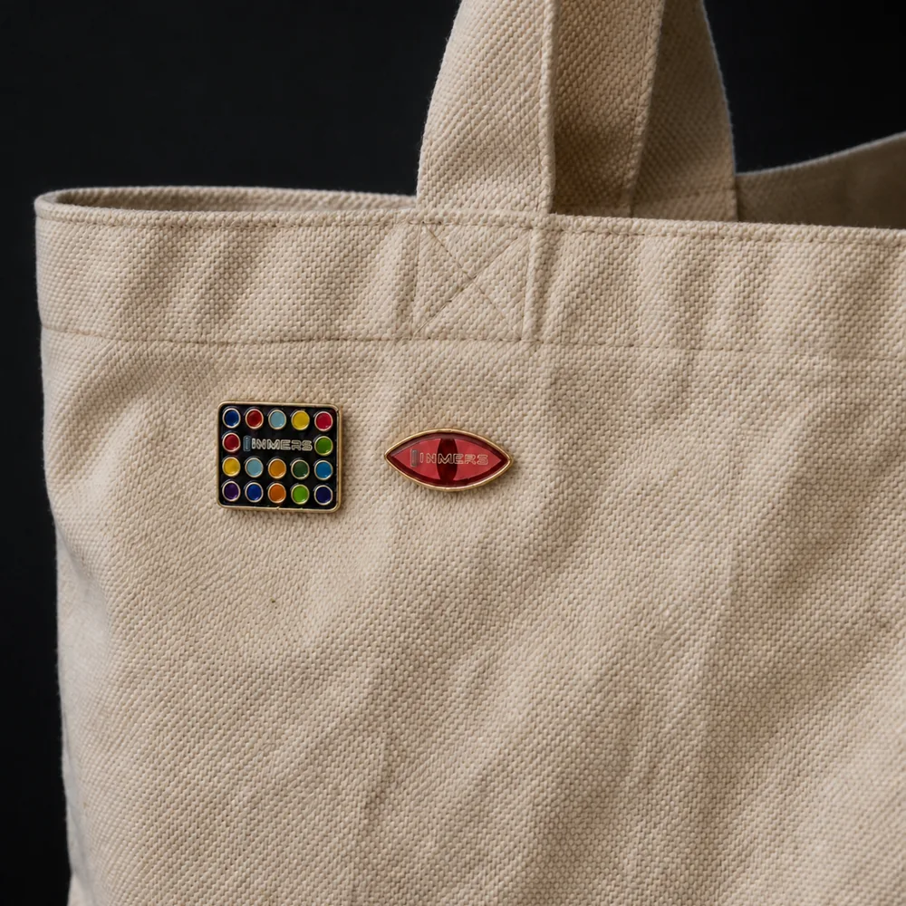 INMERS enamel pins worn on a canvas tote bag